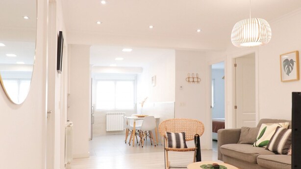 A spacious living area with a sofa, a dining table with chairs, a wicker chair, and a hanging light fixture.