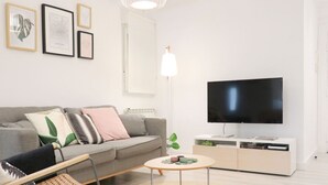 A modern living room with a grey sofa, a round coffee table, a flat-screen TV, and framed artwork on the wall.
