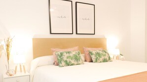 A neatly made bed with two pillows, a bedside table with a lamp, and two framed pictures on the wall.
