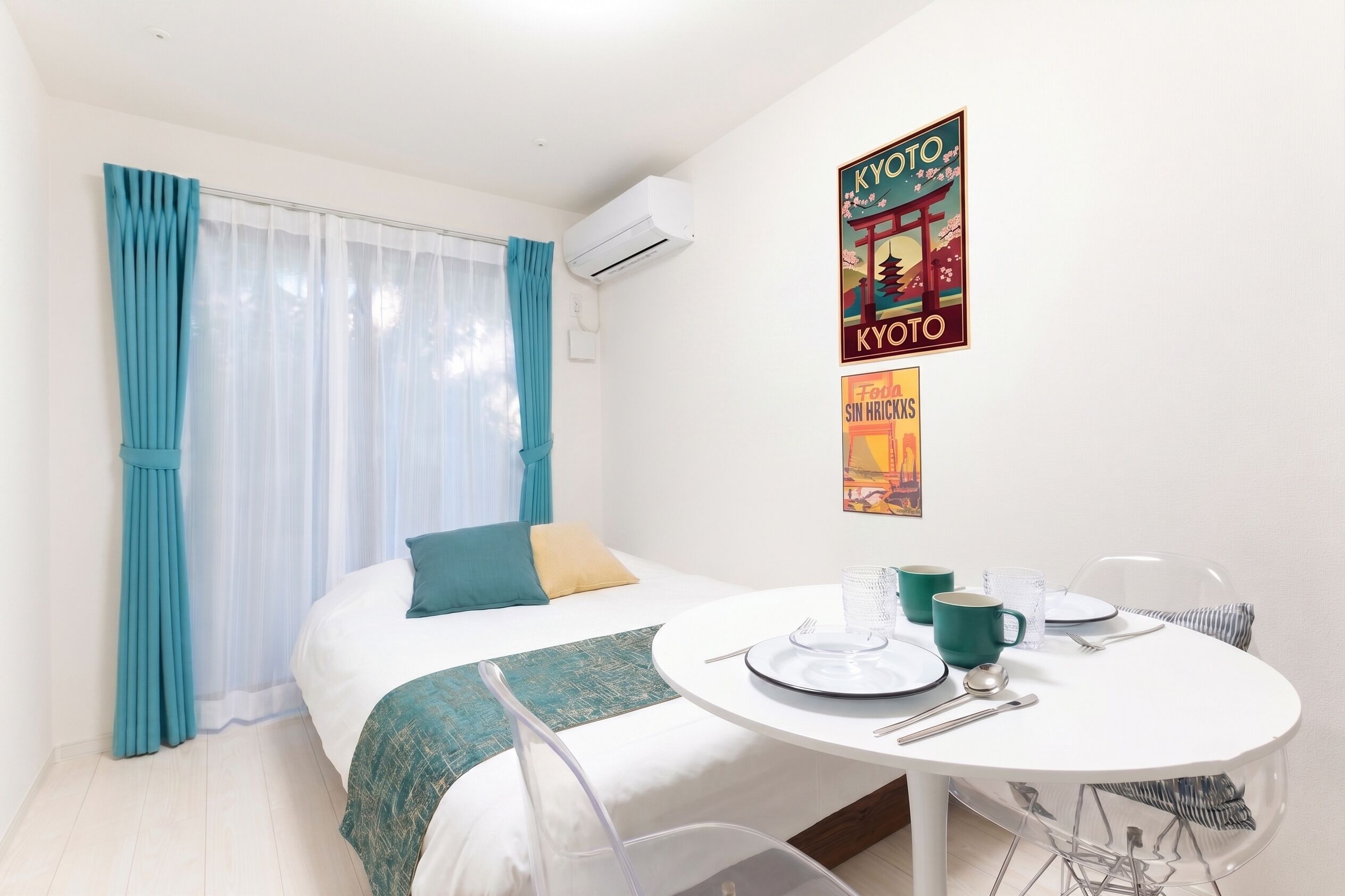 A hotel room with a bed, a dining table set for two, and a wall with two posters.
