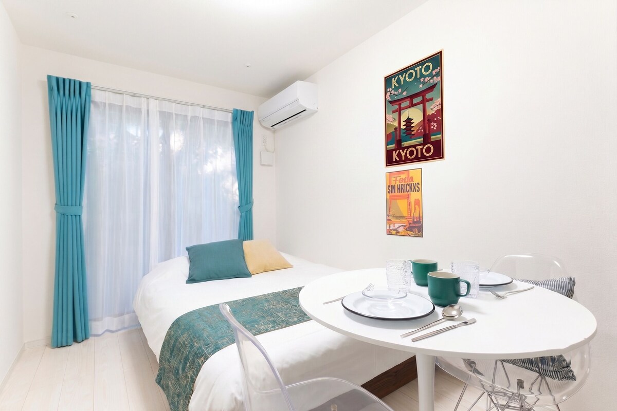 Une chambre d’hôtel avec un lit, une table à manger dressée pour deux personnes et un mur orné de deux affiches.