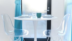 A modern room with a round white table, two clear chairs, a teal cushion, and a frosted glass window. - Flora Maison Kamiochiai by Tranova (Tokyo)