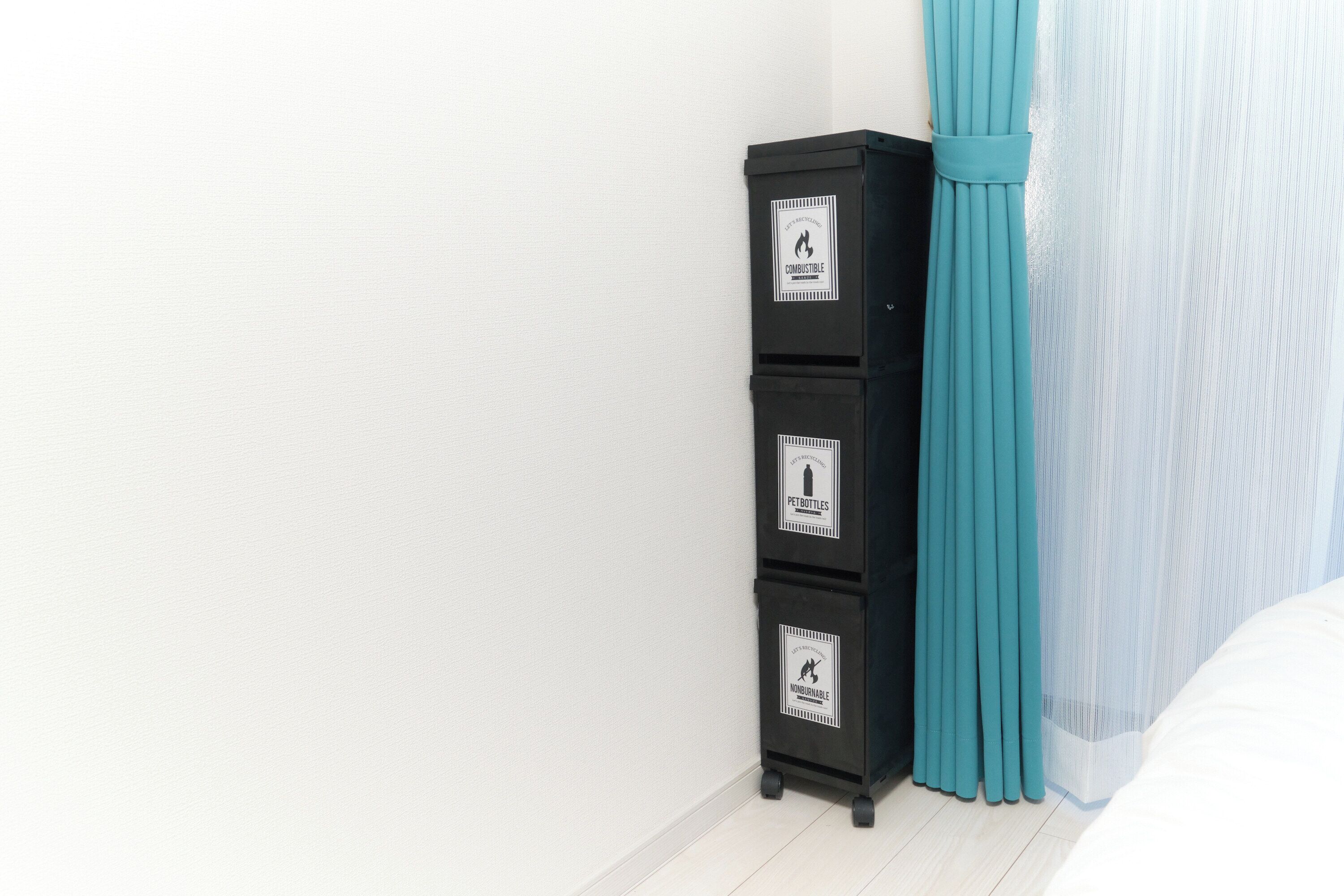Una stanza con un mobile contenitore nero, parete bianca, tende color acquamarina e un letto con biancheria da letto bianca.