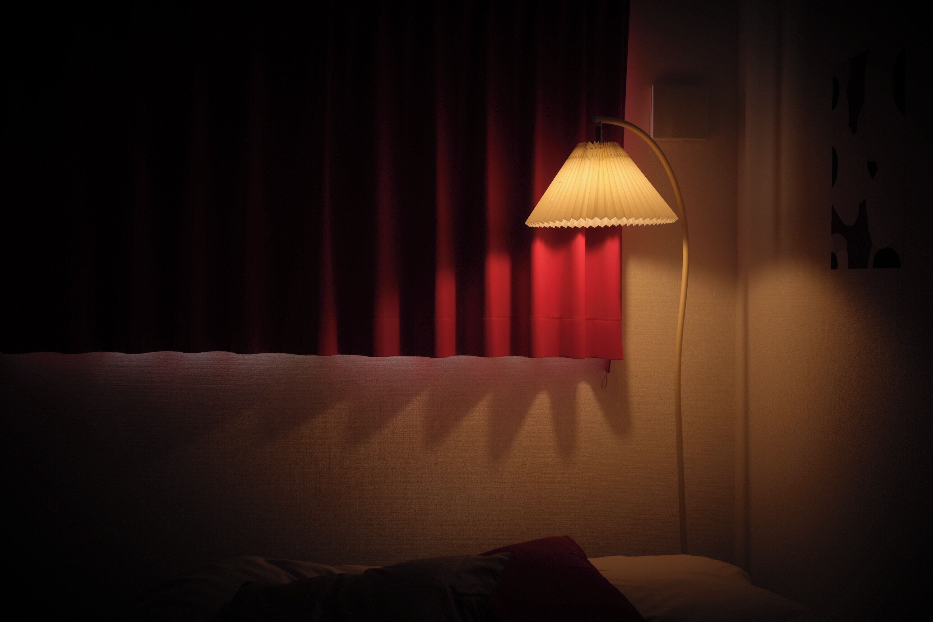 A dimly lit room with a bed, a standing lamp, and red curtains.