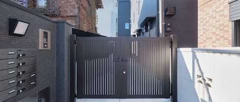 A gated entrance with a metal gate, a brick wall, and a building with a tiled facade.