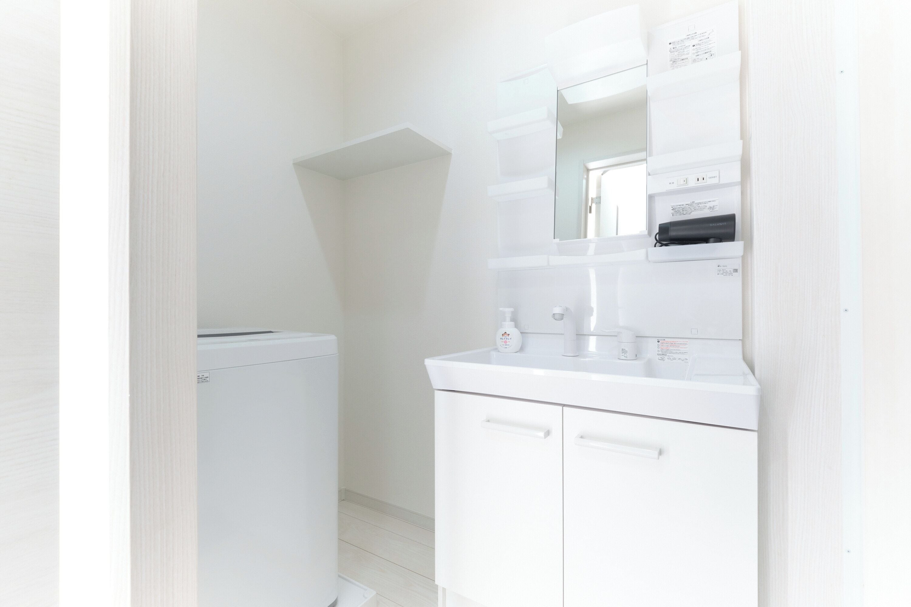 A small, white bathroom with a compact design, including a sink, mirror, and a small storage cabinet.