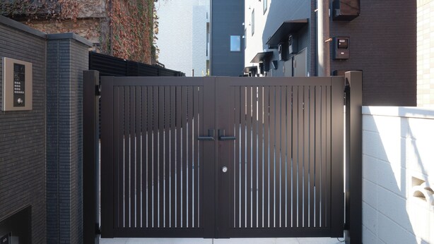 A gated entrance with a modern design, a brick wall on the left, and a white wall on the right. - Flora Maison Kamiochiai by Tranova (Tokyo)