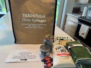 A kitchen counter with a Trädstuga bag, a can of pure maple syrup, a bag of pan mix, a green towel, and a note for guests.