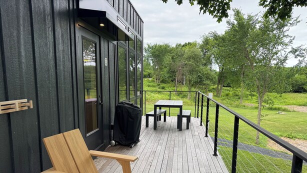Une terrasse en bois avec une table et des chaises, un barbecue et une vue sur un espace verdoyant avec des arbres.