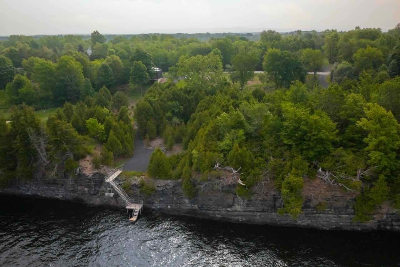 Eine Vogelperspektive auf eine natürliche Landschaft mit einer felsigen Klippe und einer hölzernen Treppe, die zu einem Gewässer hinabführt.