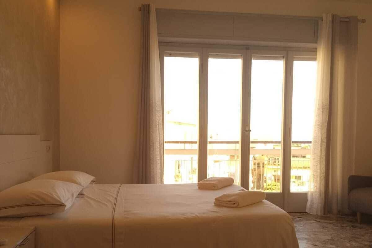 Ein Hotelzimmer mit einem großen Bett, einem Nachttisch und Blick auf die Stadt durch große Fenster.