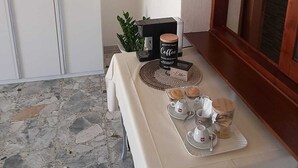 A breakfast setup with a coffee maker, a box labeled "Coffee," and a tray with cups and pastries on a table.