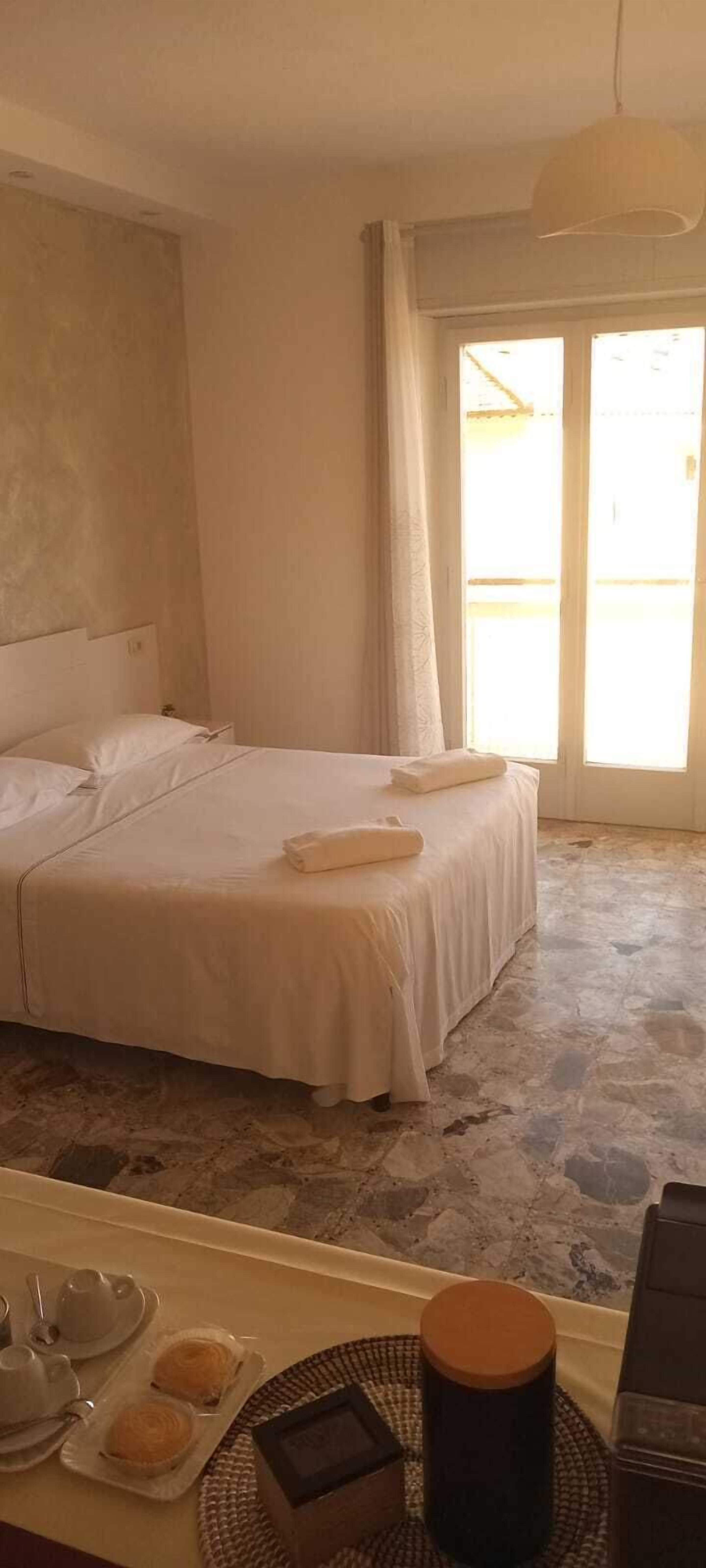 A hotel room with a bed, a breakfast table with tea and pastries, and a view of the outside through a window.