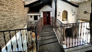 A stone-walled corridor with a wooden staircase leading to a door. - La Vigne: modernized farmhouse from 1882, incl. swimming pool (from August 2025) (Saint-Flour-l'Étang)