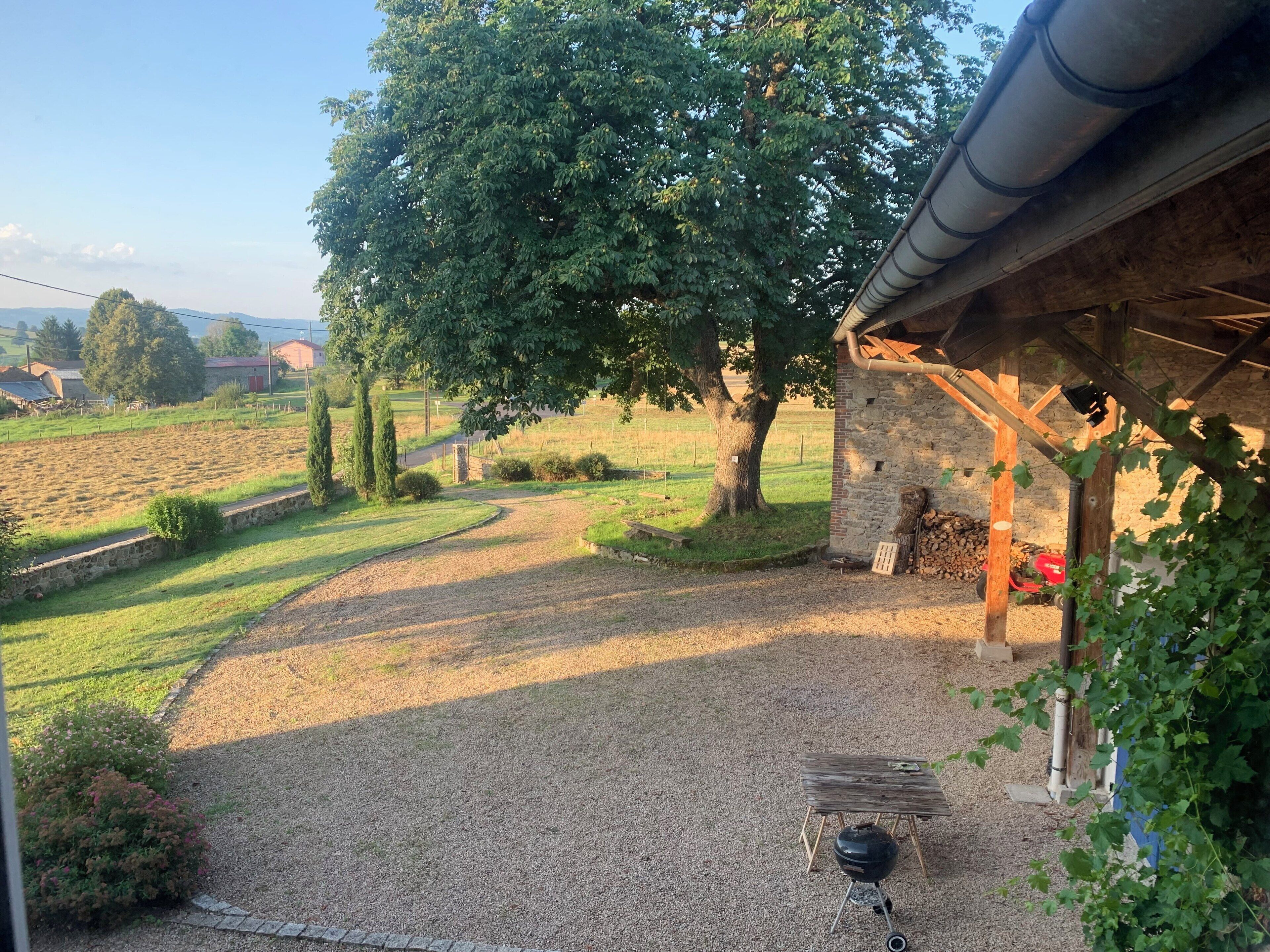 A gravel patio with a barbecue grill, a stone wall, and a wooden pergola.