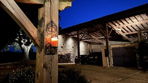 A covered outdoor area with a stone wall, a wooden pergola, and a car parked inside. - La Vigne: modernized farmhouse from 1882, incl. swimming pool (from August 2025) (Saint-Flour-l'Étang)