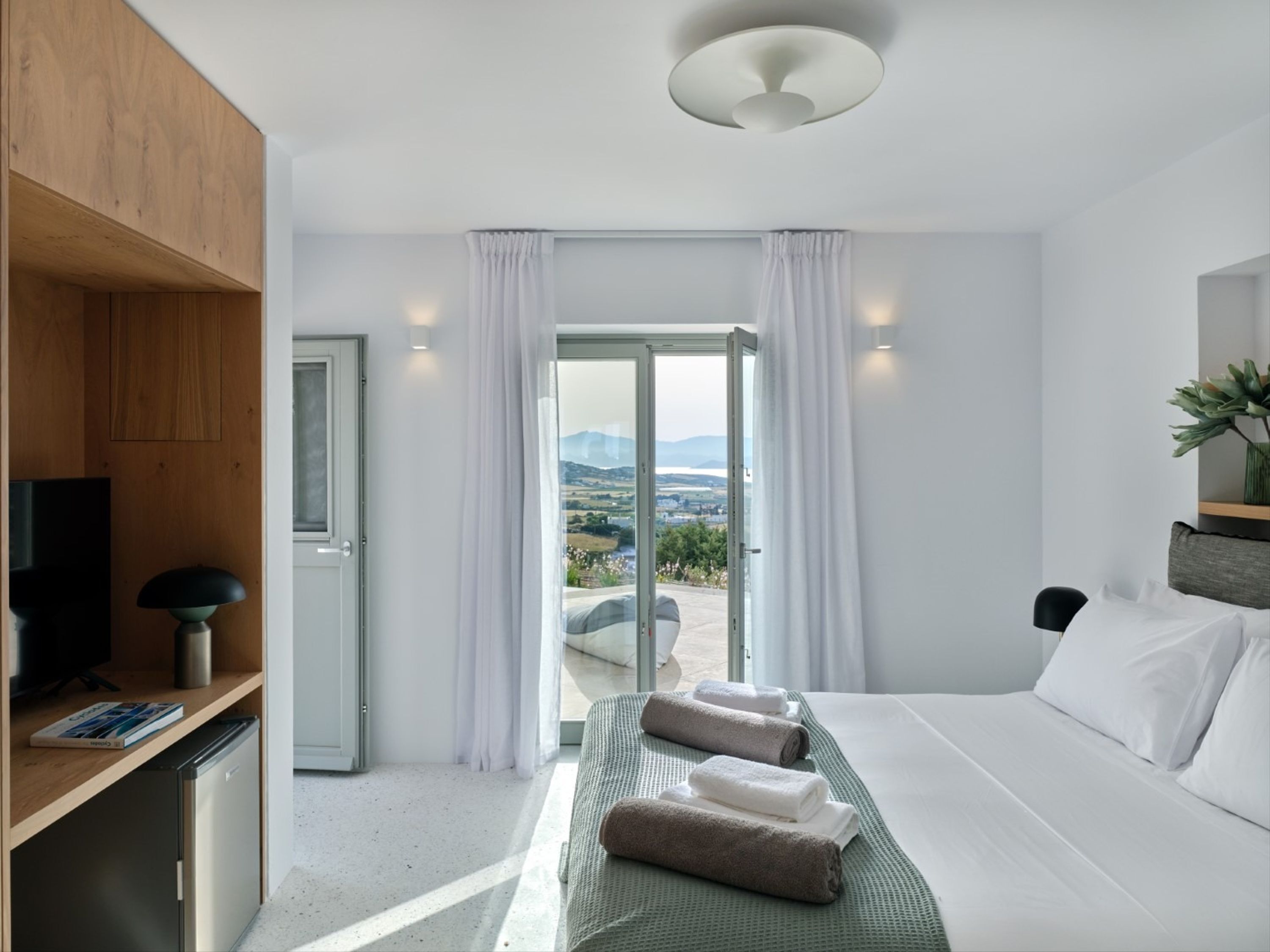 Habitación de hotel moderna con cama, escritorio con lámpara, televisión y vista al exterior.