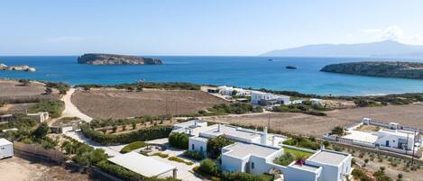 A coastal property with white buildings, a clear view of the sea, and a mountainous backdrop.