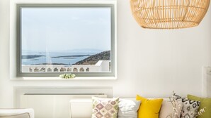 Una stanza con una grande finestra vista mare, un divano bianco con cuscini colorati e una lampada a sospensione in vimini.