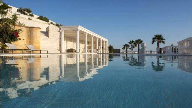 Una piscina con acqua cristallina, lettini da relax e un edificio con colonne.