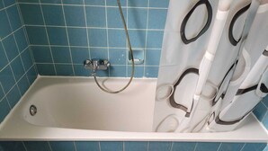 A bathtub with a showerhead, blue tiled walls, and a patterned shower curtain. - Horrem City Apartments (Kerpen)