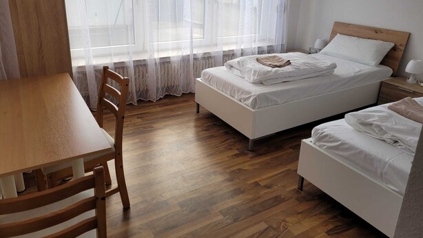 A bedroom with a wooden floor, a bed with white bedding, a wooden nightstand, and a chair. - Horrem City Apartments (Kerpen)