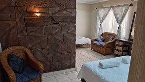 A room with a stone wall, a wicker chair, a bed with a white bedspread, and a window with sheer curtains. - La'Mathil (Enormwater AH)