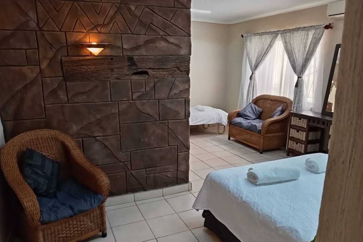 A room with a stone wall, a wicker chair, a bed with a white bedspread, and a window with sheer curtains.