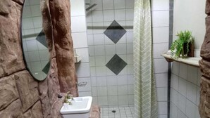 A bathroom with a stone wall, a sink, a shower, and a mirror. - La'Mathil (Enormwater AH)