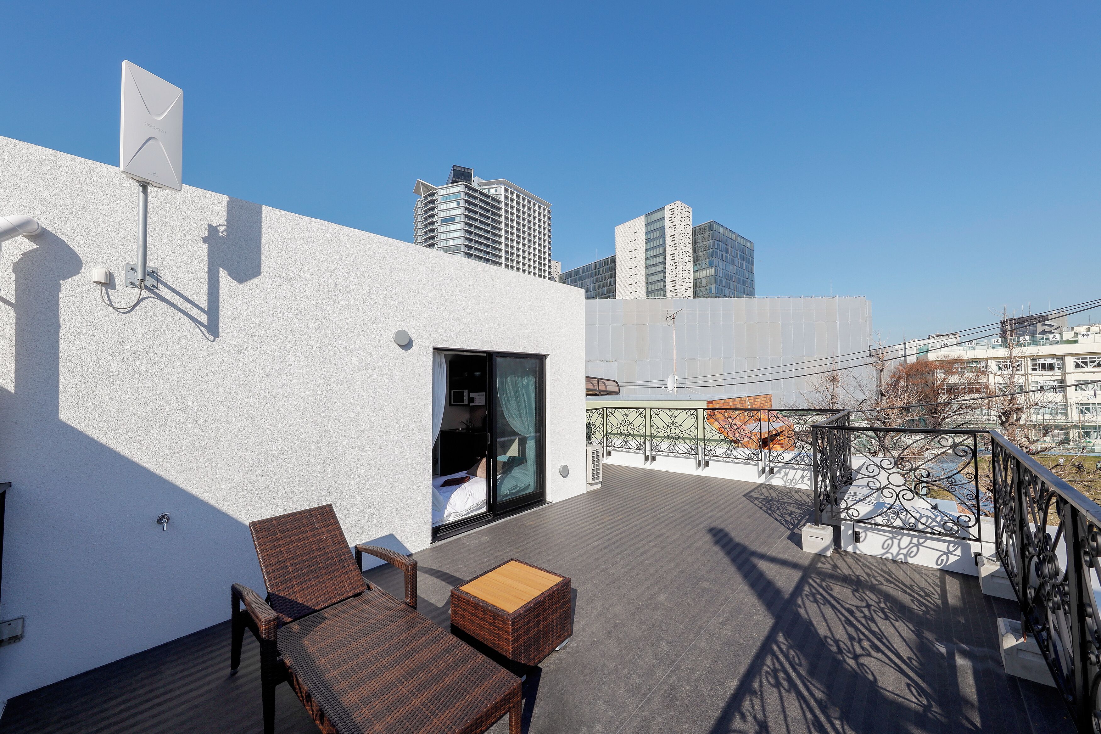 A rooftop terrace with a white wall, a glass door entrance, and a metal railing.