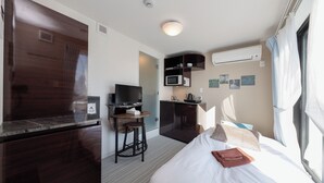 Una camera d'albergo con un letto, una scrivania con una sedia, un forno a microonde e una TV.
