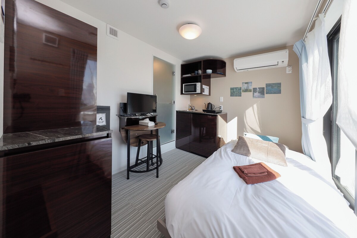 Una camera d'albergo con un letto, una scrivania con una sedia, un forno a microonde e una TV.