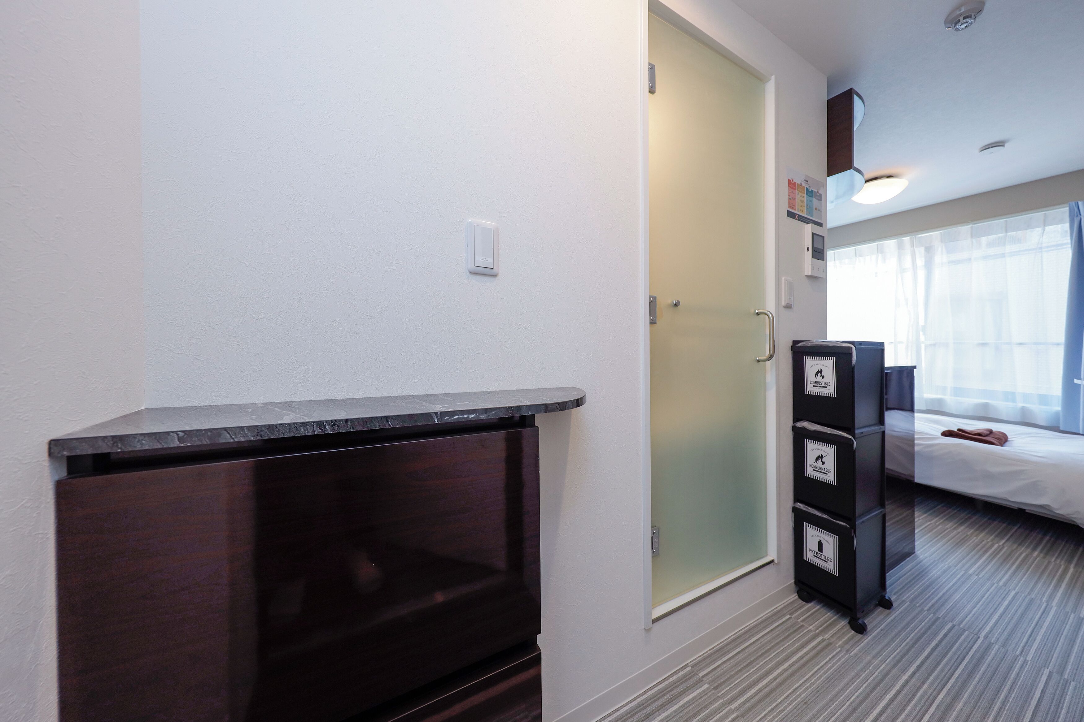 Une chambre d’hôtel compacte avec un meuble en bois foncé, une petite kitchenette, un lit avec un rideau bleu et une fenêtre ornée de rideaux légers.