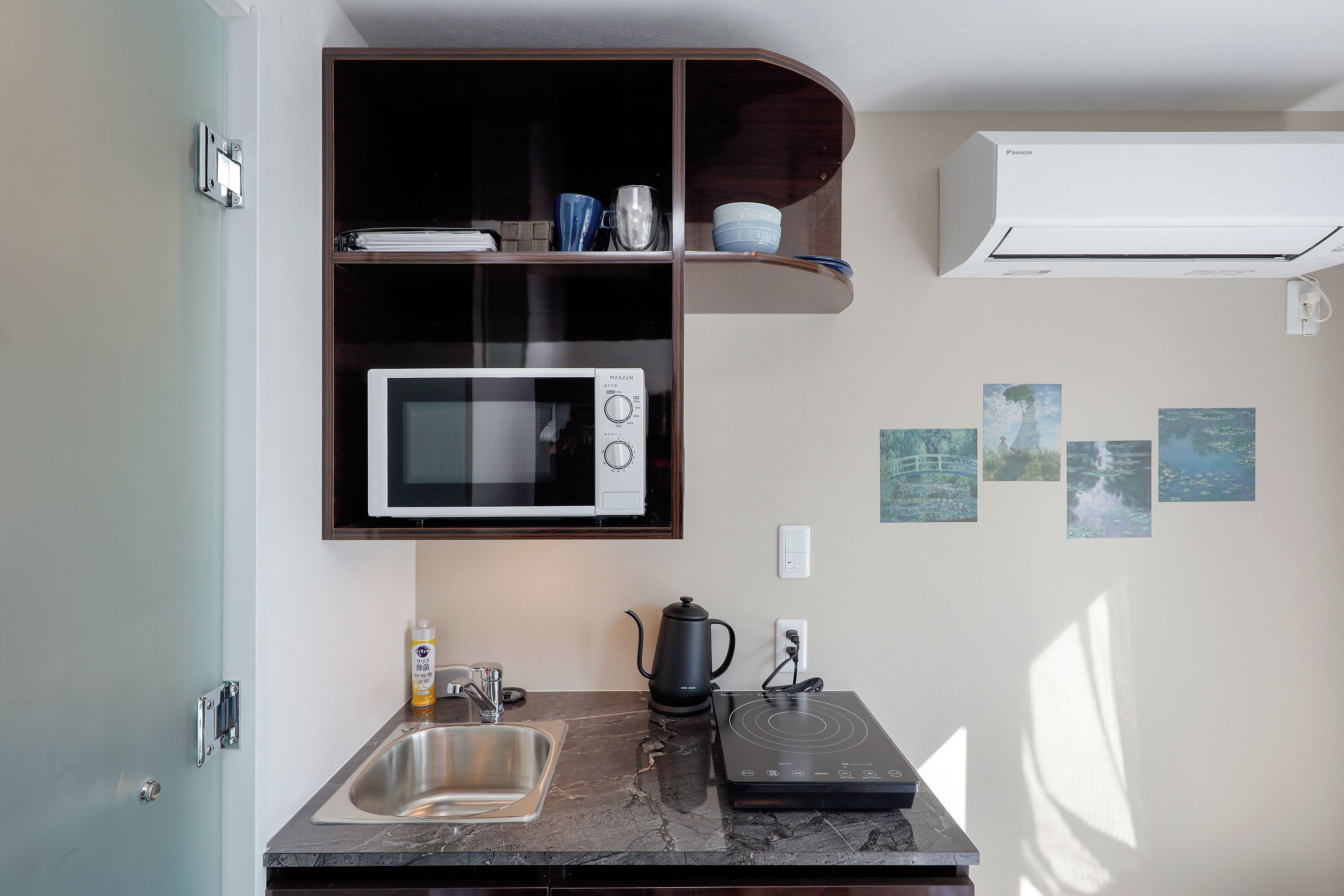 Una cocina compacta con microondas integrado, hervidor y lavabo.