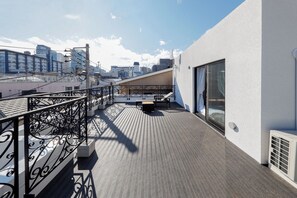 A rooftop terrace with a metal railing, a concrete bench, and a view of the cityscape. - Ra Grande by Tranova (Tokyo)