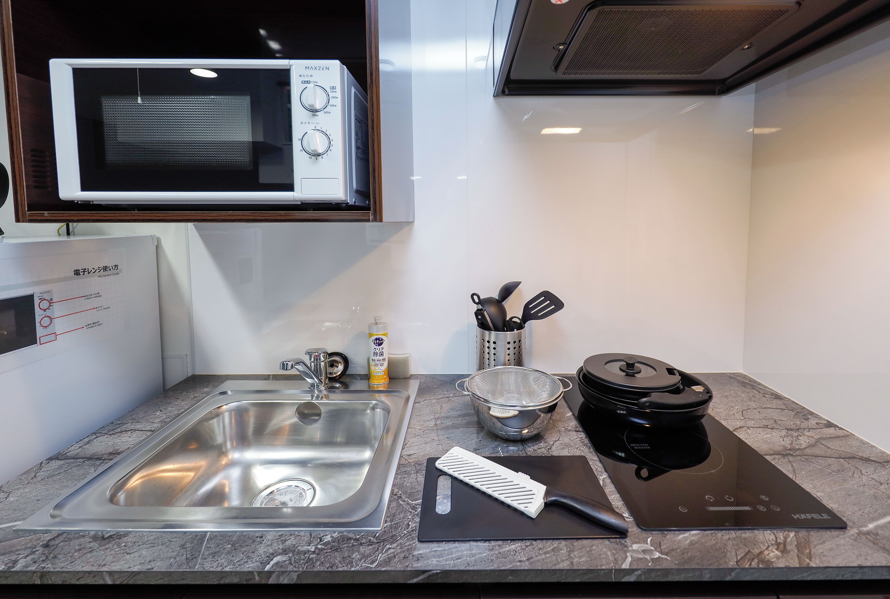 Una cocina con un lavamanos de acero inoxidable, un microondas, una cafetera y un hervidor sobre la encimera.