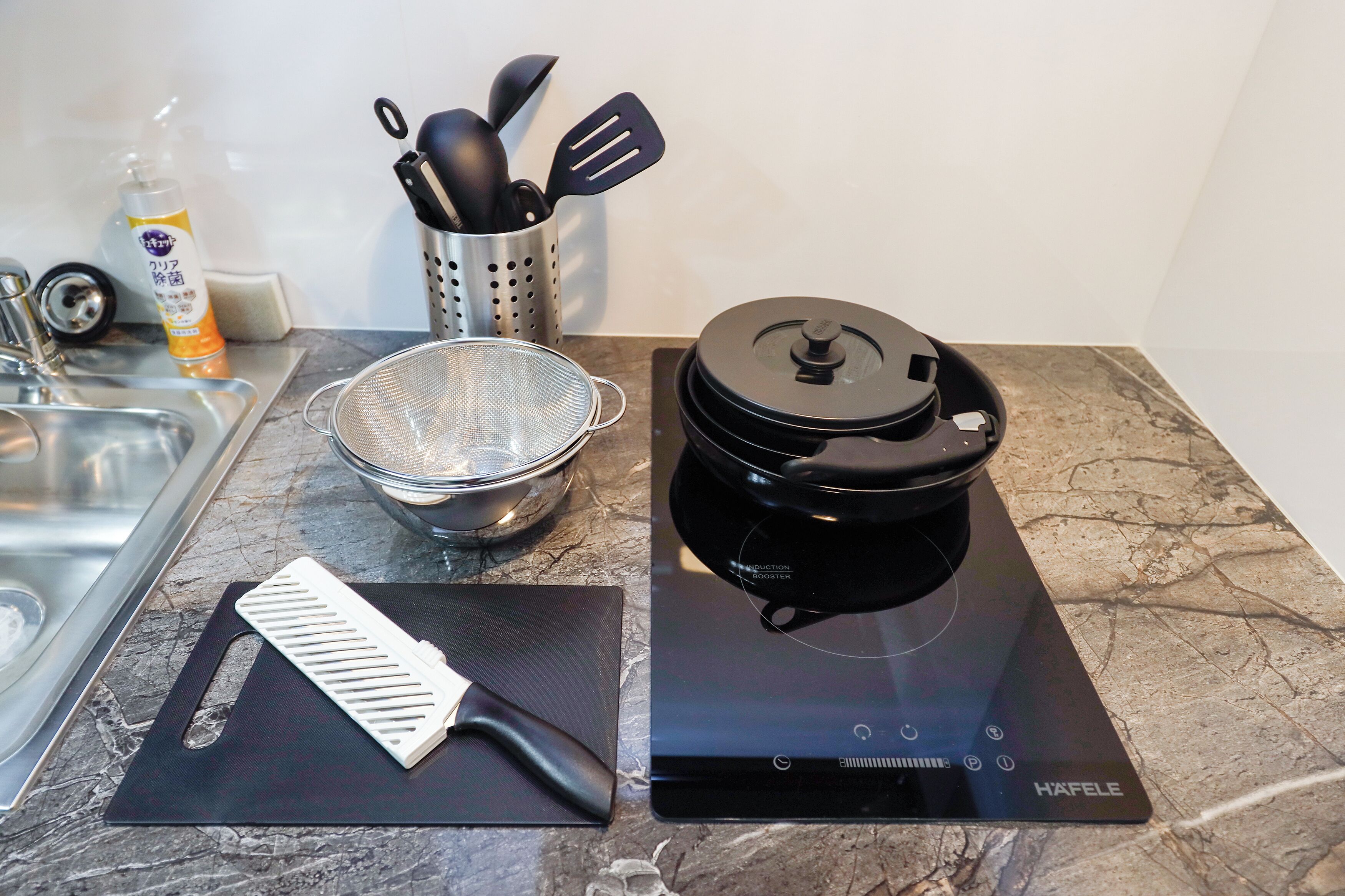 A kitchen counter with a black induction cooktop, a strainer, a spatula holder, and a bottle of cooking oil.