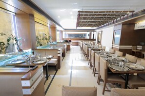 Um restaurante amplo com mesas compridas, cadeiras e um balcão central com vitrine.