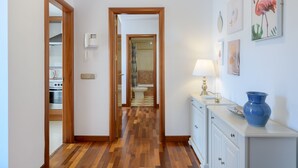 A hallway with wooden flooring, a white cabinet, a blue vase, and a wall-mounted phone. - SUITE YAGABO - ARRECIFE - LANZAROTE (Arrecife)