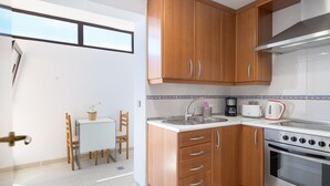 A kitchen with wooden cabinets, a stove, and a dining area with a table and chairs. - SUITE YAGABO - ARRECIFE - LANZAROTE (Arrecife)