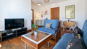 A living room with a TV, sofa, coffee table, and a dining area with a table and chairs. - SUITE YAGABO - ARRECIFE - LANZAROTE (Arrecife)
