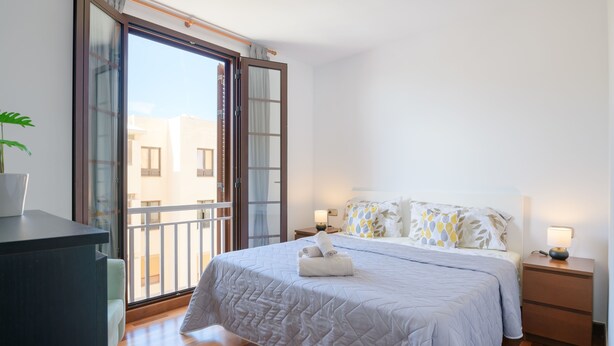A bedroom with a large bed, a nightstand, a desk, and a sliding glass door leading to a balcony. - SUITE YAGABO - ARRECIFE - LANZAROTE (Arrecife)