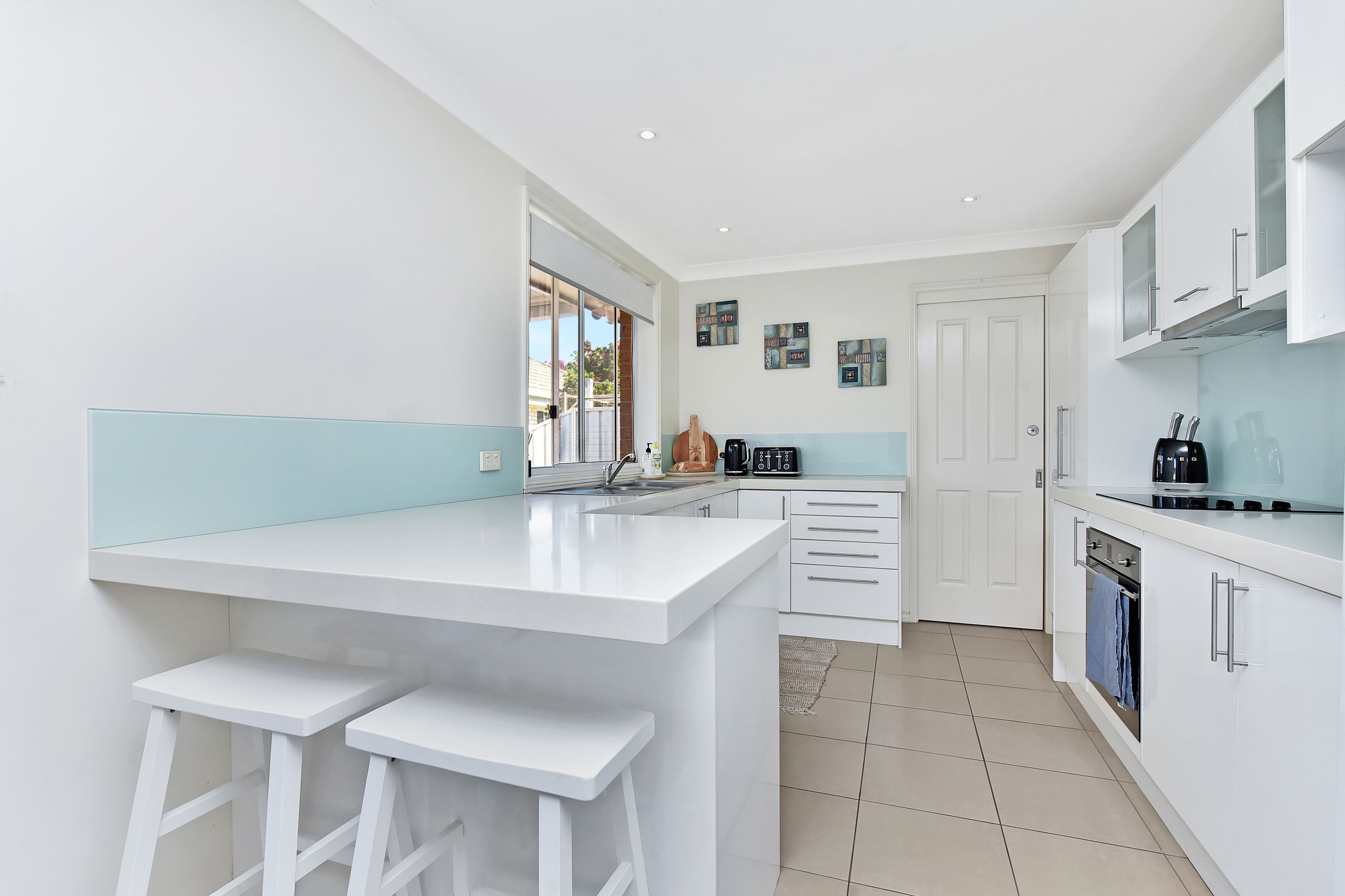 A modern kitchen with white cabinetry, a central island with bar stools, a built-in oven, and a coffee machine.