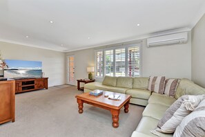 A living room with a television, sofa, coffee table, and a view of the sea through the window.