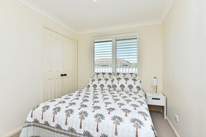 Une chambre à coucher avec un lit, une table de chevet, une lampe et une fenêtre avec des stores.