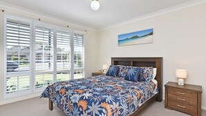 A bedroom with a large bed, a nightstand, a dresser, and a window with blinds.