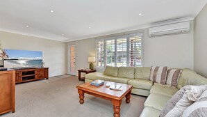 A living room with a sofa, coffee table, TV, and a large window with blinds.