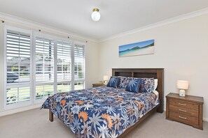Een slaapkamer met een groot bed, een nachtkastje, een lamp en een schilderij van een strand.