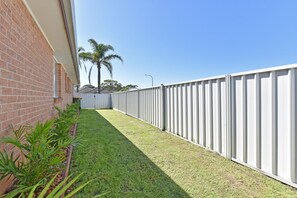 A fenced outdoor area with a grassy lawn, a brick wall, and a palm tree.