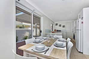Een moderne keuken met een eethoek, witte kastjes en een grote schuifpui naar een terras.
